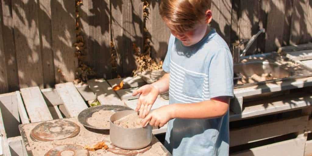 A mud kitchen with mixing bowls, old pots and pans, wooden spoons and storage space